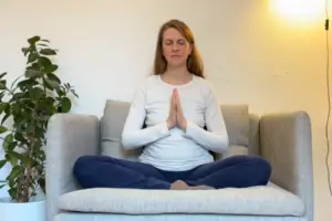 Die Yogalehrerin Anna Sophie Pietsch sitzt im Schneidersitz auf einem Sessel und hat die Hände im Anjali Mudra.