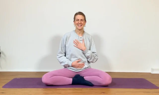 Die Yogalehrerin Anna Sophie Pietsch sitzt auf einer Yogamatte und lacht mit geschlossenen Augen.