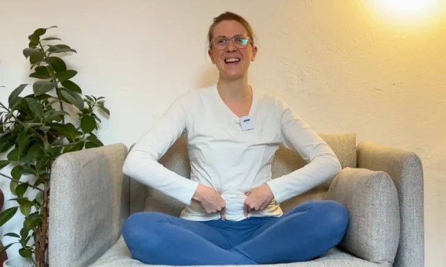 Die Yogalehrerin Anna Sophie Pietsch lacht in die Kamera und zeigt auf ihren Bauch